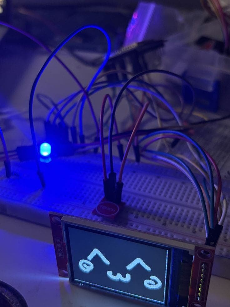Breadboard build with a small screen showing a cute face, lit by a blue LED