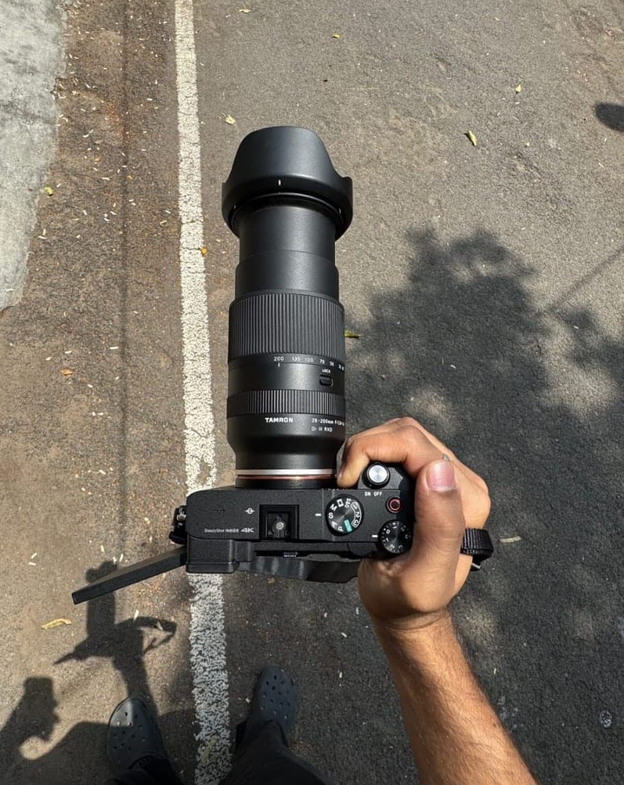 Holding a mirrorless camera with a long zoom lens over a sunlit road